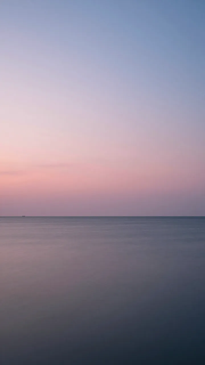 Long exposure vertical view of a calm sea beneath a soft pink and blue dusk sky