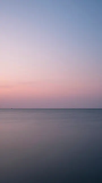 Long exposure vertical view of a calm sea beneath a soft pink and blue dusk sky