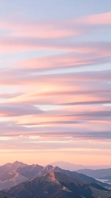 Layered pastel lenticular clouds stretch above rugged mountain peaks at soft dusk