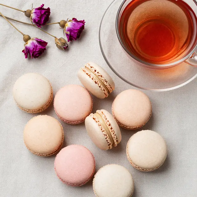 Overhead view of pastel macarons, rose tea and dried roses on a linen napkin