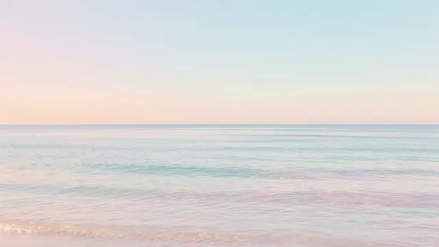 Calm pastel gradient sky meets gentle pale ocean waves along a quiet horizon