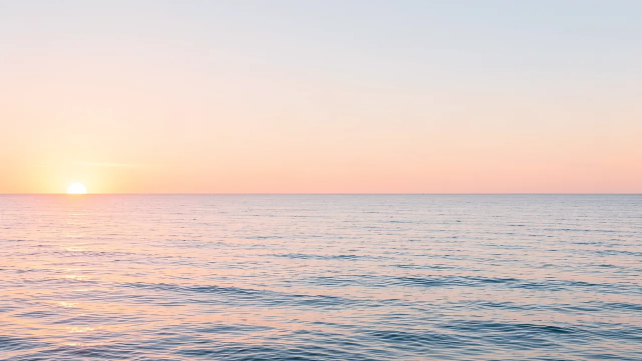 Low sun at the left horizon casts soft pastel light over calm, gentle ocean waves under an open sky