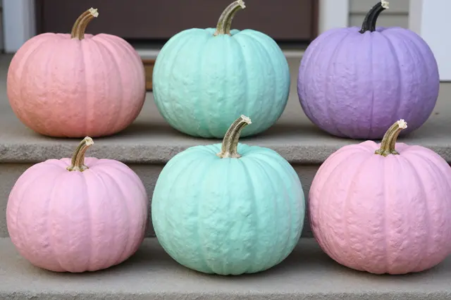 Arranged pink, mint, and lilac painted pumpkins sit neatly on concrete porch steps