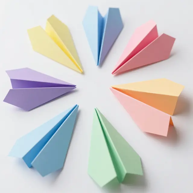 Top view of pastel colored paper airplanes arranged in a circle on a plain white background