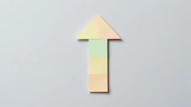 An upward-pointing arrow assembled from small pastel paper pieces sits on a pale gray background