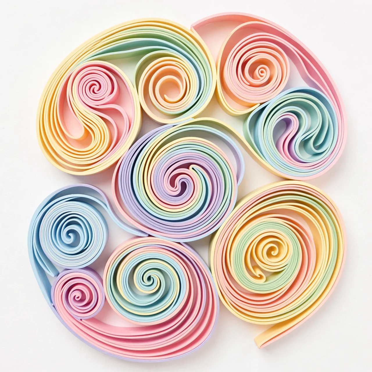 Intricate rolled pastel paper quilling swirls arranged on a plain off-white background