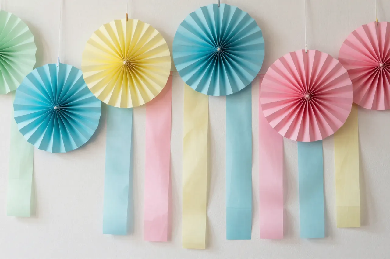 Hanging pastel pleated paper fans and matching streamers arranged against a plain light wall