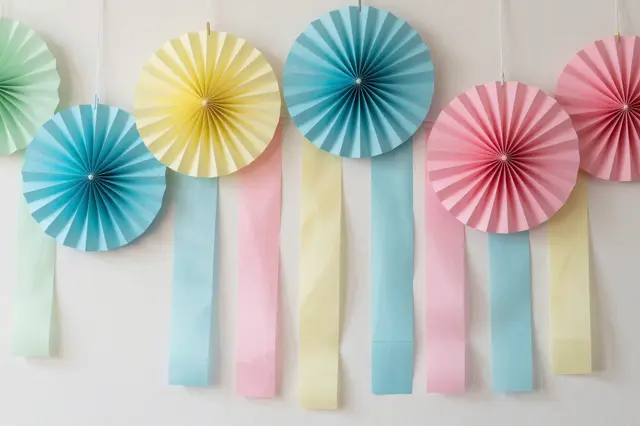 Hanging pastel pleated paper fans and matching streamers arranged against a plain light wall