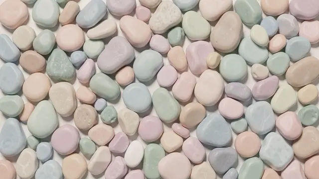 Smooth rounded pebbles in soft muted pastel tones scattered across a pale neutral base