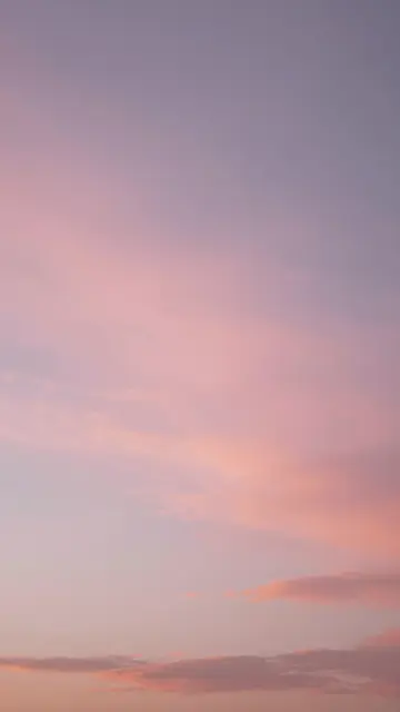 Vertical view of a soft gradient sunset sky filled with wispy pink and purple clouds