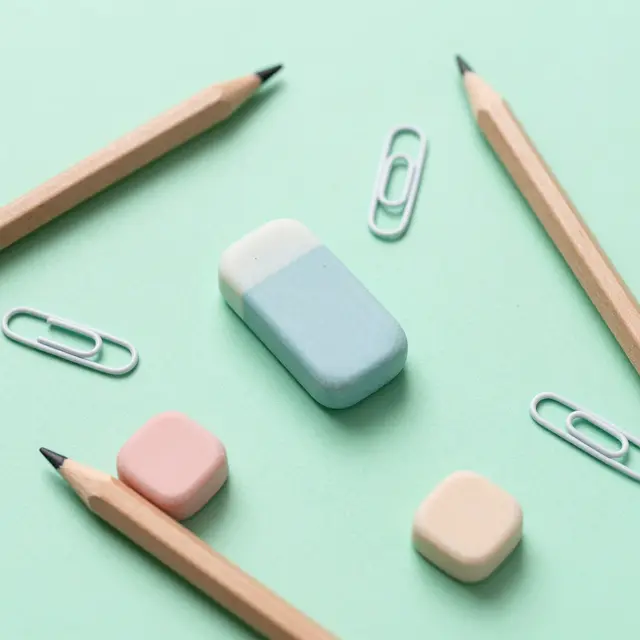 Erasers, wooden pencils and white paper clips arranged on a mint green paper surface