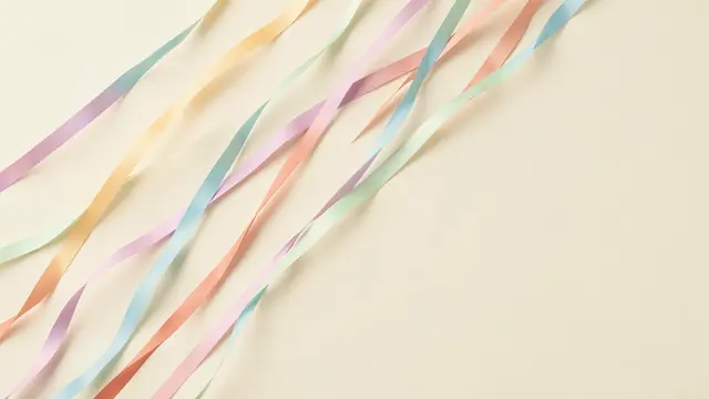 Twirling diagonal pastel paper streamers lie across a cream backdrop with empty copy space on the right