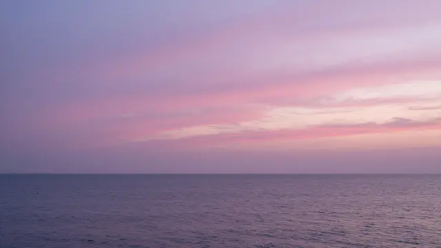 Pink and purple streaked twilight sky sits over a calm, gently rippled ocean horizon.