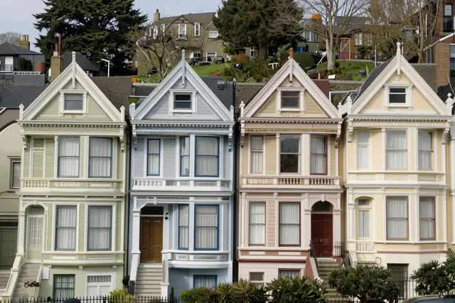 Four ornate pastel Victorian houses stand in a row on a sloped residential hill
