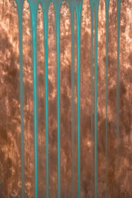 Full frame close-up of weathered copper with vertical turquoise patina drip streaks