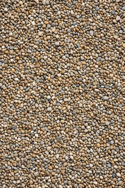 Full frame top view of small rounded pea gravel stones in tan, cream and gray tones.