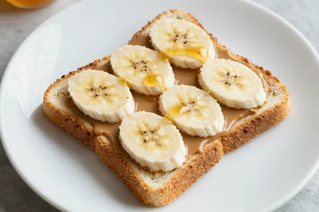 Top-down view of toast topped with peanut butter, banana slices and honey drizzle on a white plate