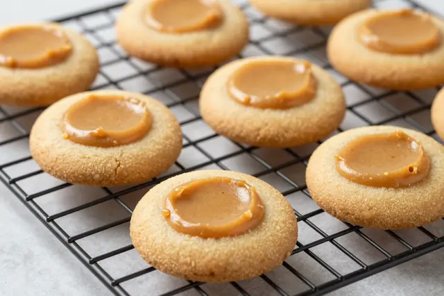 Thumbprint peanut butter cookies rest on a black wire cooling rack over a light countertop.