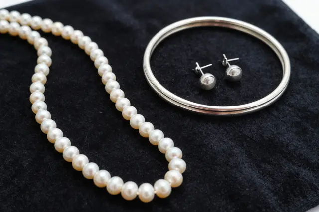 Pearl strand, silver bangle and stud earrings arranged on a dark velvet surface