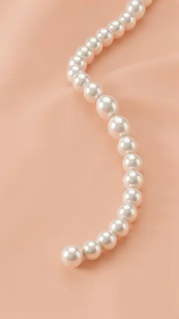 A curved strand of glossy white pearl beads rests on soft draped peach fabric.