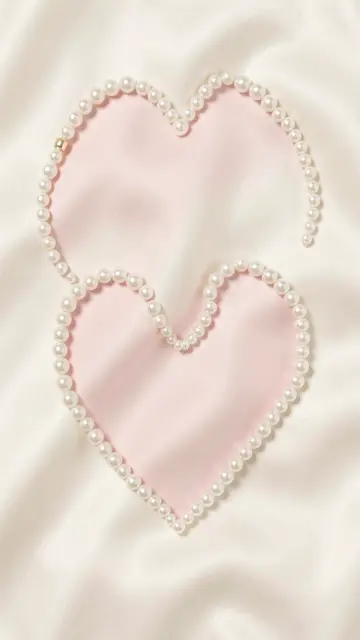 Two hearts shaped from pearl strands rest on soft draped ivory silk over pale pink fabric.