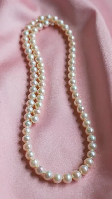Coiled pearl necklaces rest gently on soft draped pink silk fabric.