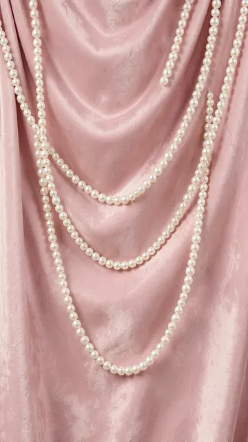 Layered white pearl strands draped softly over folded blush pink velvet fabric