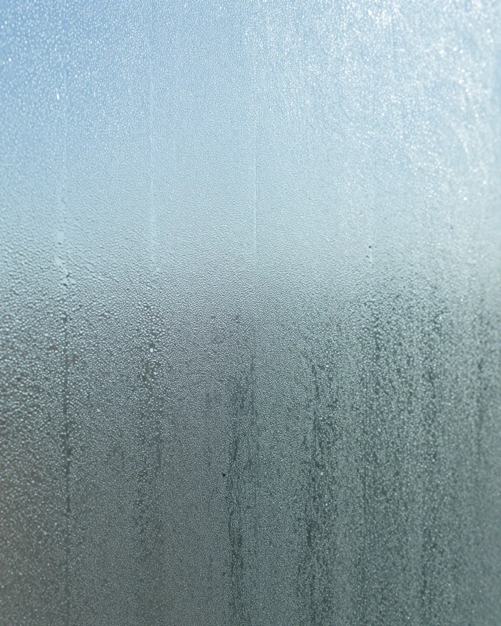 Close-up of pebbled privacy glass with condensation and soft cool blue daylight behind the surface