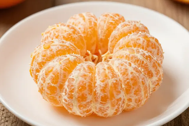 A fully peeled segmented orange arranged in a flower shape rests on a white plate over a wooden table