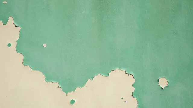 Close-up of a wall with peeling mint green paint revealing an underlying cream paint layer
