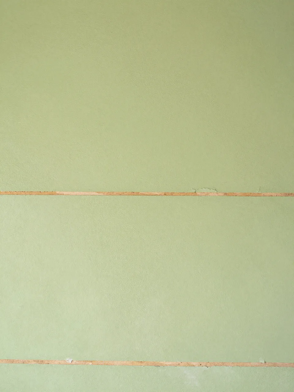 Full frame close-up of pale green plaster with horizontal cracks revealing thin wooden lath strips