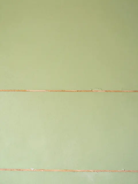 Full frame close-up of pale green plaster with horizontal cracks revealing thin wooden lath strips