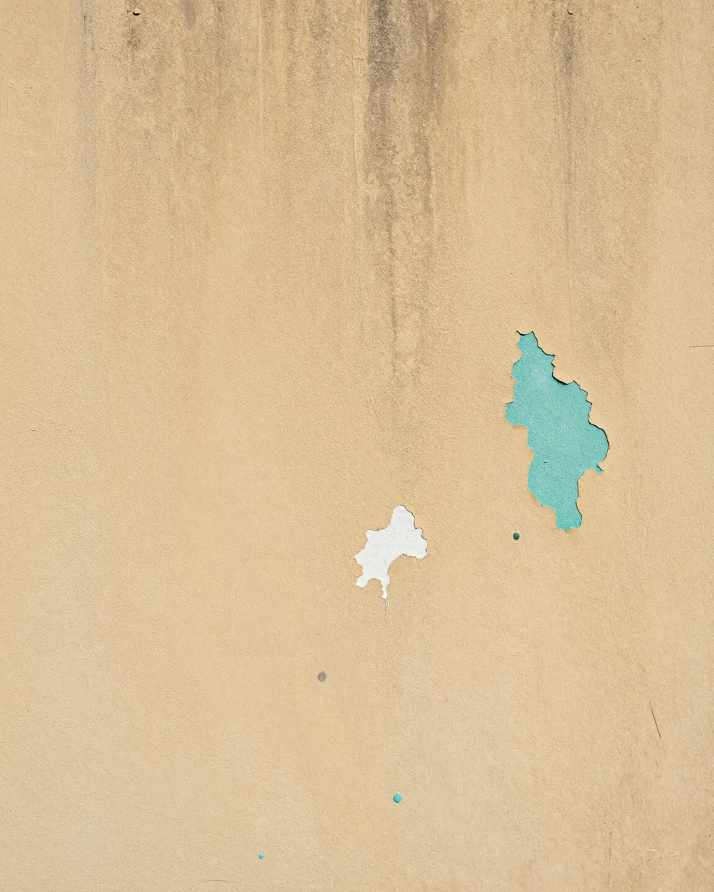 Close-up of a weathered plaster wall with chipped paint revealing teal and white underlayers