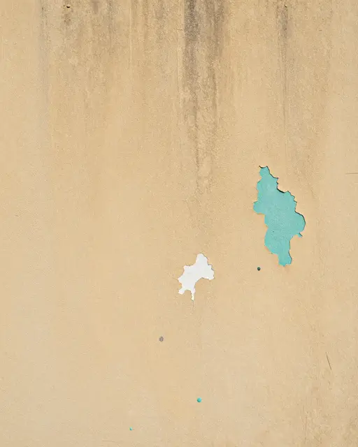 Close-up of a weathered plaster wall with chipped paint revealing teal and white underlayers