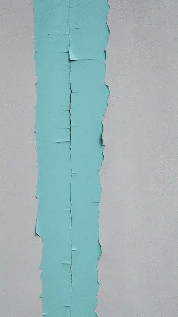 Close-up of a wall with flaking cracked teal paint over smooth gray plaster surface