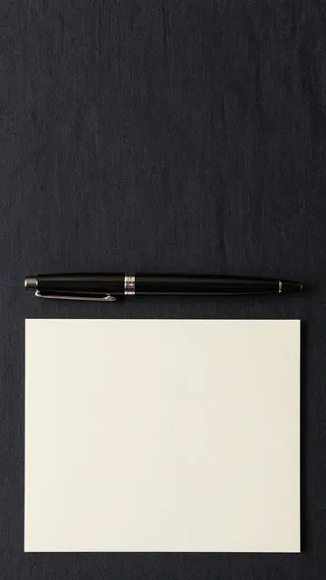 A black pen rests above a blank cream card on dark linen fabric with empty vertical space above.