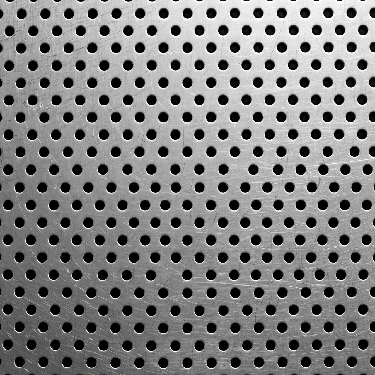 Full frame close-up of brushed perforated stainless steel with uniform round holes over a dark background