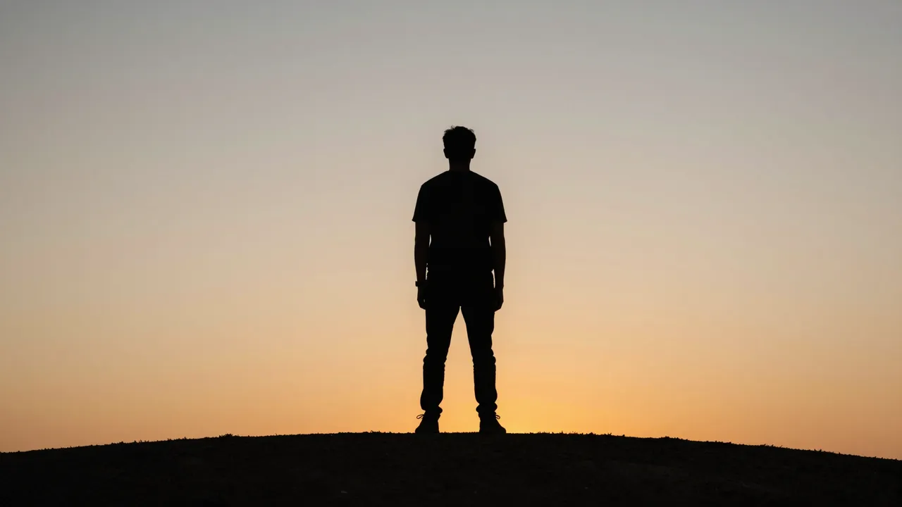 A dark silhouette of a standing person on a hill against a warm gradient sunset sky