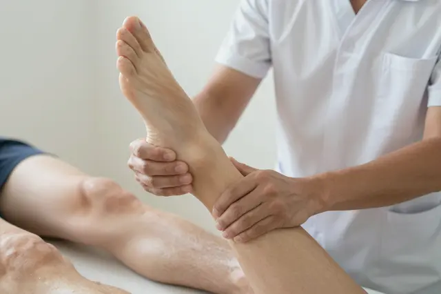 A physiotherapist holds and supports a patient's foot and ankle during a physical therapy session.