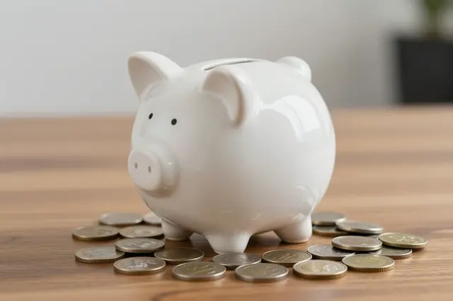 White ceramic piggy bank surrounded by scattered coins sitting on a wooden desk