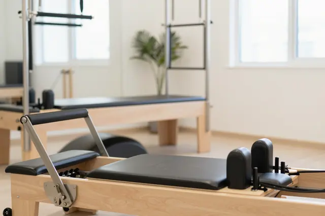 Wooden pilates reformer machines arranged in a sunlit minimalist exercise studio