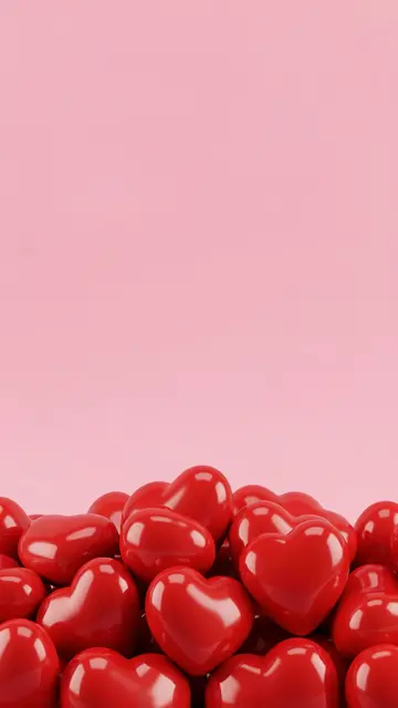 Glossy red 3D hearts are stacked along the bottom edge of a soft solid pink vertical background with empty copy space above.