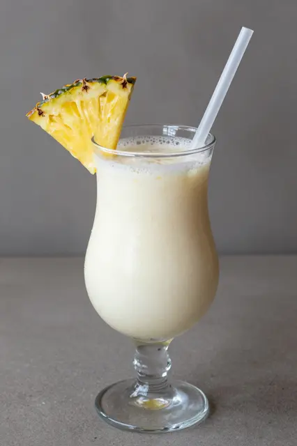 Creamy pina colada in a hurricane glass garnished with a pineapple wedge and plastic straw