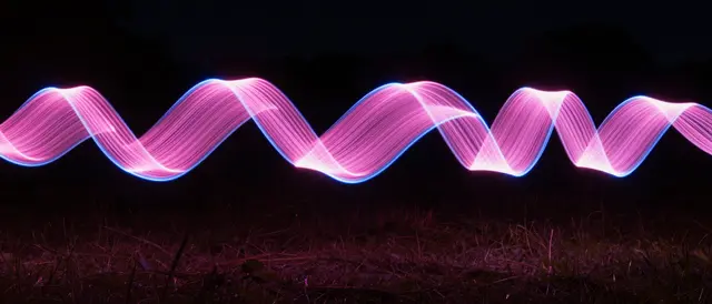 Twisted wavy pink and blue light ribbons stretch across a dark night grass field