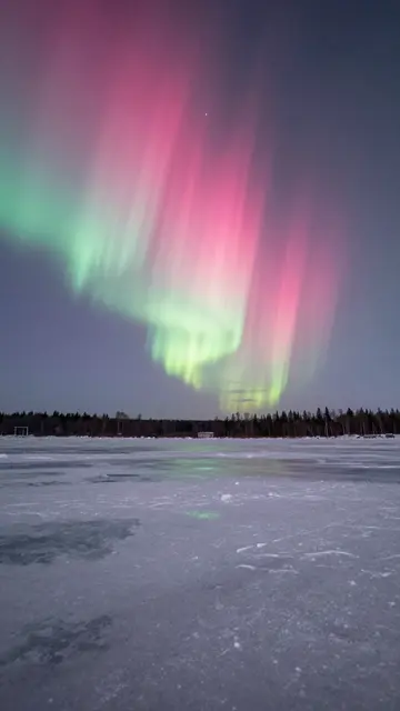 Vibrant pink and green aurora borealis streaks across the night sky above a frozen lake
