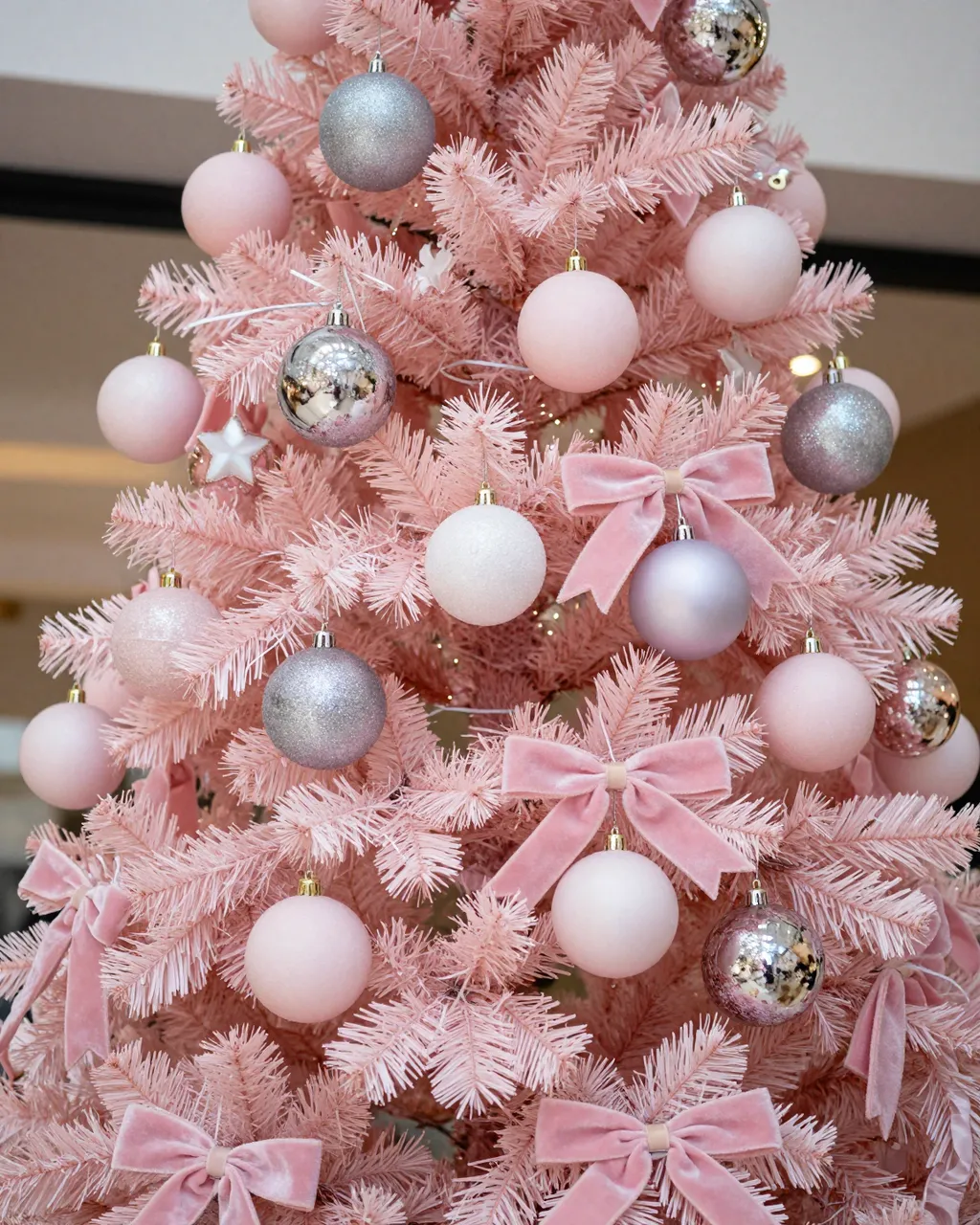 Close-up of a pink artificial Christmas tree decorated with pastel baubles and velvet pink ribbon bows