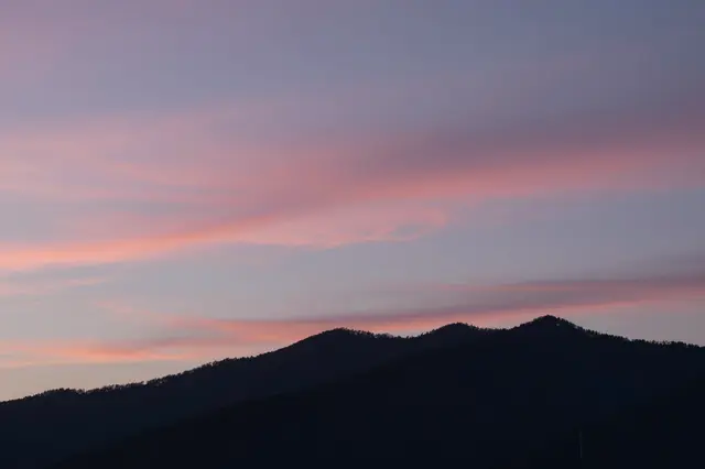 Soft streaked pink cirrus clouds drift above a dark mountain silhouette at early dawn