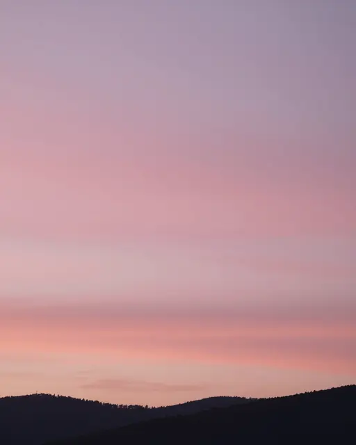 Soft gradient pink and lavender dusk sky above dark silhouetted hilltops