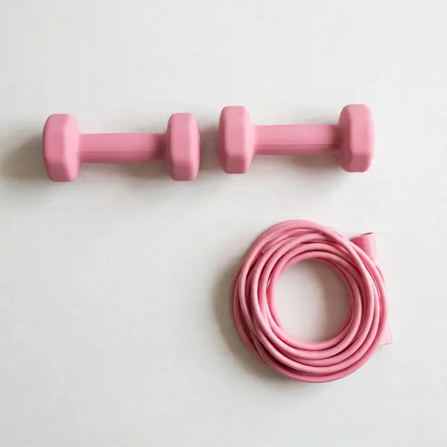 Overhead view of two small pink dumbbells and a coiled pink jump rope resting on a plain white floor