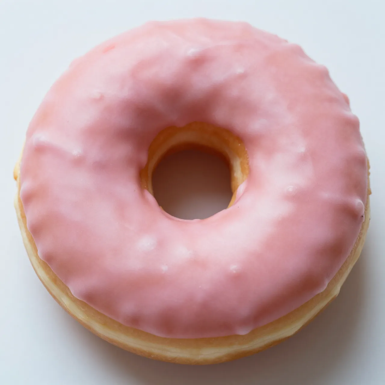 A top-down close-up of a donut coated in smooth light pink icing on a plain light background